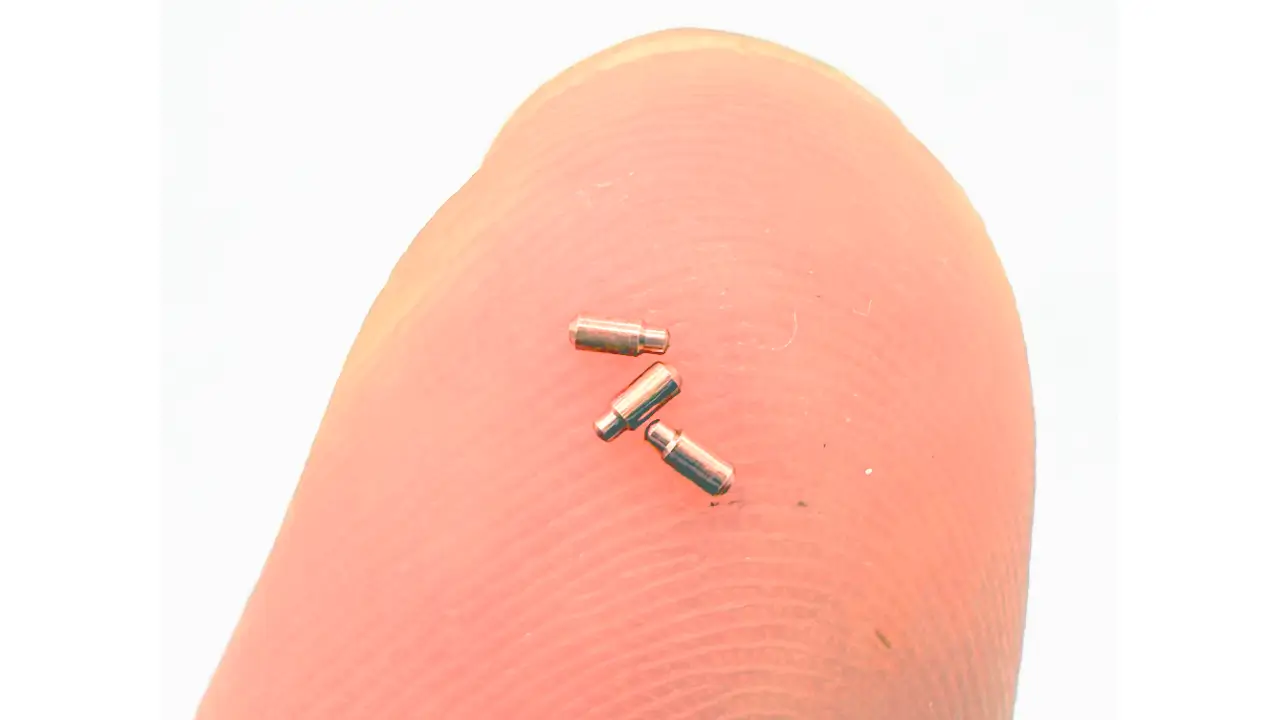 Ultra-small copper parts (Ø0.68 mm) displayed on fingertip for scale.